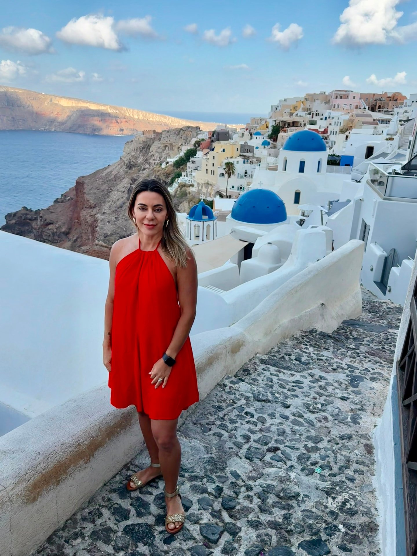 Carolina Andrade em Oia, Santorini, com as casas brancas e cúpulas azuis ao fundo